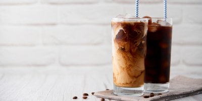 Ledová káva ve vysoké sklenici se smetanou na bílém dřevěném pozadí