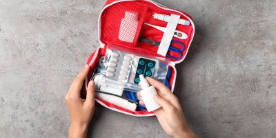 Žena vkládá do otevřené lékárničky nosní sprej, v lékárničce jsou nůžky, teploměr, léky