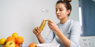 Mladá žena loupe ovoce, zatímco sedí doma u stolu