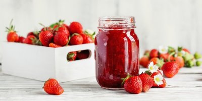 Doma vyráběná jahodová marmeláda ve sklenici a kolem čerstvé jahody