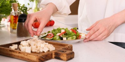 Člověk si do salátu přidává nakrájený sýr feta