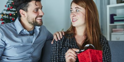 Žena si zaskočeně prohlíží vánoční dárek od svého partnera