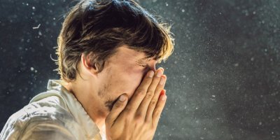 Muž kýchá do dlaní a kolem něj se víří prach