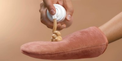 Ruka aplikuje samoopalovací krém na dlaň chráněnou rukavicí