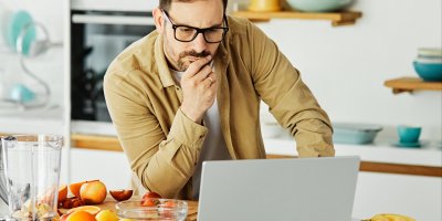 Muž se kouká do notebooku, vedle sebe má mixér a ovoce