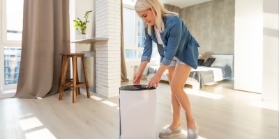 Žena mačká tlačítko na čističce vzduchu, která je umístěna uprostřed místnosti