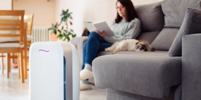 Žena si čte na gauči, vedle ní spí pes a před nimi je čistička vzduchu