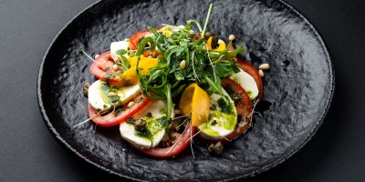 Salát caprese s rukolou a oříšky na černém talíři