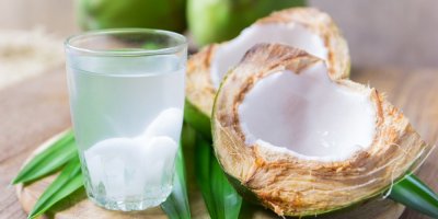 Kokosová voda ve sklenici vedle rozpůleného kokosu