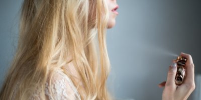 Žena si stříká parfém směrem na blonďaté vlasy