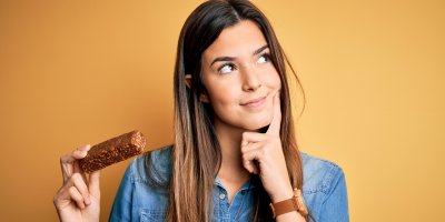 Žena se tváří zamyšleně a v ruce drží domácí proteinovou tyčinku