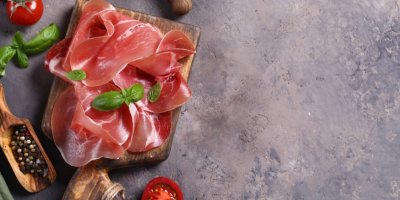 Sušená šunka na dřevěném podnose s rajčaty a bazalkou 