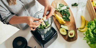 Žena dává do mixéru banán, připravené má avokádo a špenát