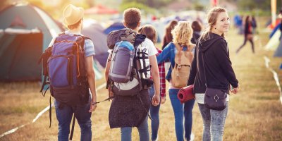 Skupina přátel s kempovací výbavou kráčí mezi stany