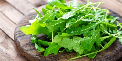 Orosené lístky rukoly na dřevěném prkénku