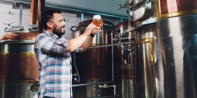 Muž si prohlíží sklenici s pivem vedle pivovarnických kádí