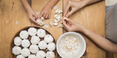 Dospělý a dítě loupou česnek, několik česneků na tácu