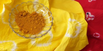 Červeně a žlutě batikovaná látka a na ní miska s kurkumou