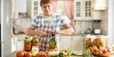 Žena v kuchyni zavařuje zeleninu, jako jsou rajčata, okurky, papriky