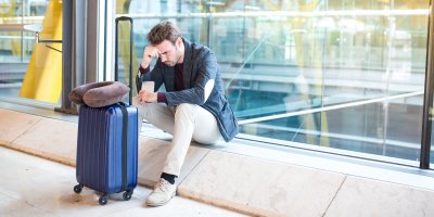 Zoufalý muž sedící s kufrem na letišti