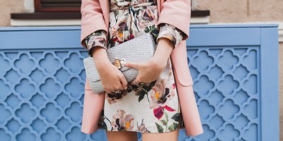 Žena v elegantních květovaných šatech a růžovém prodlouženém sáčku drží velkou, stříbrnou kabelku