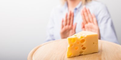 Žena rukama naznačuje odmítnutí, před ní je kus ementálu na prkénku