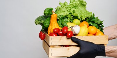 Ruce v rukavicích držící bedýnku s ovocem a zeleninou