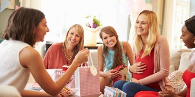 Žena předává dárkovou tašku těhotné kamarádce, kolem sedí další tři ženy