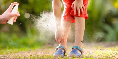 Stříkání repelentu na nohy dítěte, kolem kterého poletují komáři