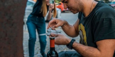 Muž zkouší otevřít láhev vína zavíracím nožem.