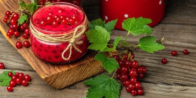 Zavařený rybíz ve skleničce na dřevěném tácu a kolem čerstvý rybíz