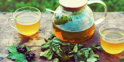 Rybízový čaj v konvici a kolem lístky a čerstvý rybíz