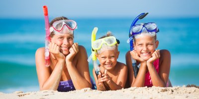 Trojice dětí ležících se šnorchly a potápěčskými maskami na pláži