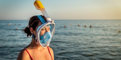 Žena s celoobličejovou šnorchlovací maskou stojící u moře