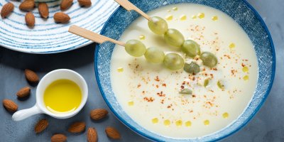 Polévka ajoblanco, ve které jsou dva špízy s hroznovým vínem, vedle je olej a mandle