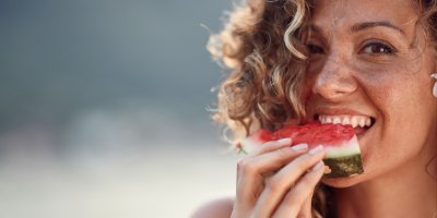 Žena s kudrnatými vlasy ukusuje meloun