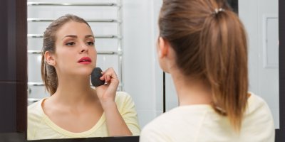 Žena si před zrcadlem odličuje obličej konjakovou houbičkou