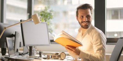 Muž držící knihu a smějící se v kanceláři