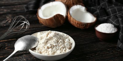 Rozpůlený kokosový ořech, kokosová mouka v misce, lžíce, metlička