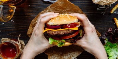 Ruce držící hovězí hamburger s kečupem, cibulí, salátem a dalšími ingrediencemi