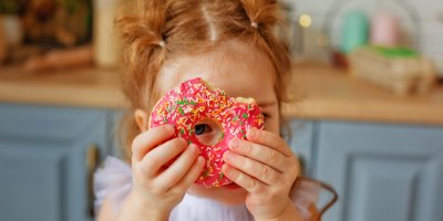 Holčička držící donut s růžovou polevou a barevným posypem