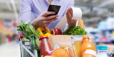 Muž v supermarketu kouká na účtenku a do mobilu