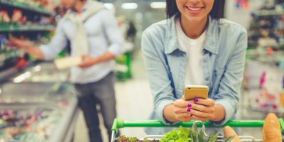 Žena drží mobil při nakupování v supermarketu