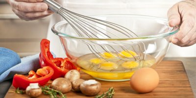 Paprika, houby a skleněná mísa s vejci, které jde kuchař šlehat metličkou