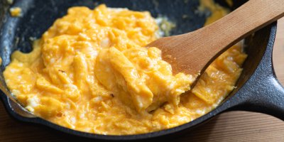 Míchaná vejce na pánvi s dřevěnou obracečkou