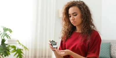 Žena s kudrnatými vlasy si přístrojem měří hladinu cukru v krvi z prstu