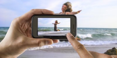 Ruce fotí na mobilu skákající ženu na pláži