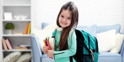 Dívka s batohem na zádech a školními potřebami v náručí