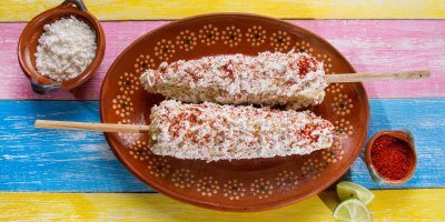 Dva kusy elotes na ozdobném talíři, sýr, limetka, chilli