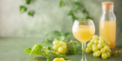 Burčák ve sklenici, v pozadí hrozny